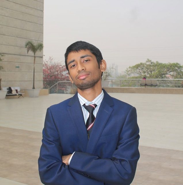 Portrait of MT Ekleel, standing outdoors in a blue suit with arms crossed